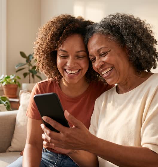 A mother and her adult daughter laugh together at the gift card that has just arrived on her phone.
